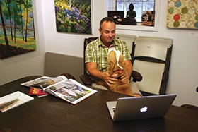 Traven Pelletier sits at a desk in his office at Bloom Garden Center in Dexter, Michigan. A dog jumps in his lap.