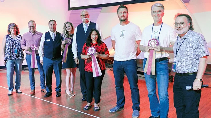 A group of people stand in an auditorium in a line, some holding prize ribbons