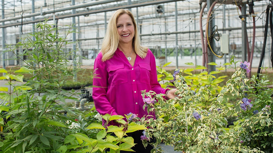 A woman in a hot pink shirt stands among plants in a greenhouse.