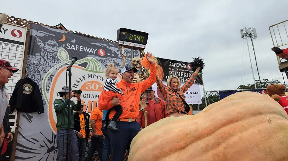 Several people stand and celebrate in front of a massive orange pumpkin on a stage.