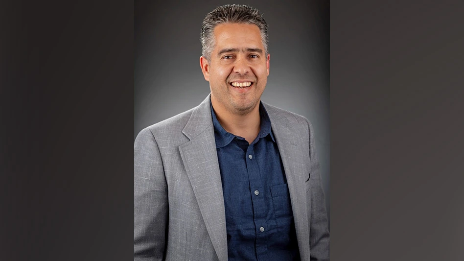 A smiling man wearing a navy blue dress shirt and gray suit jacket poses for a professional headshot photo.