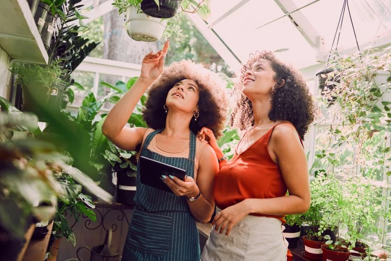 A garden center employee carrying an iPad points to a plant to show a customer.