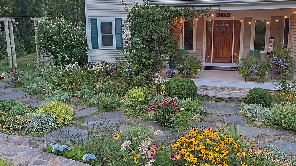 A garden in front of a house is filled with flowers and plants.