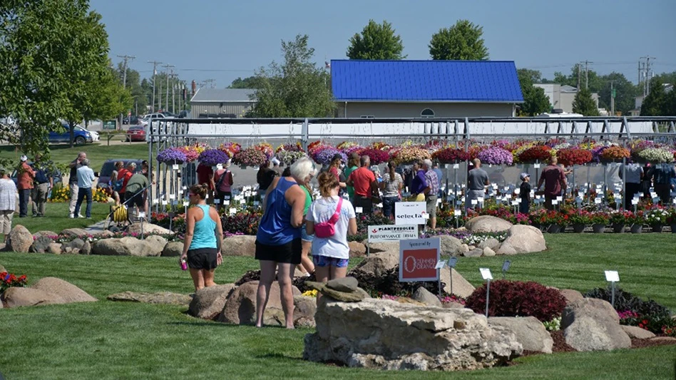 People walk in a garden full of plants on the ground and hanging baskets.