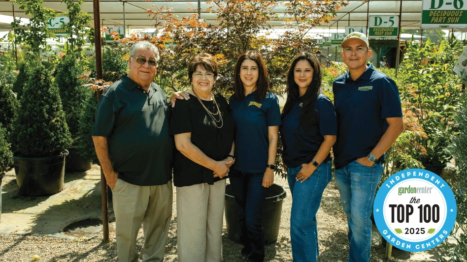 Five smiling people pose for a photo in a greenhouse.