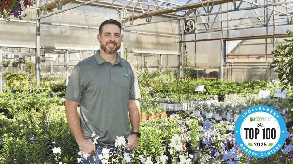 A smiling man standing in a greenhouse surrounded by plants.