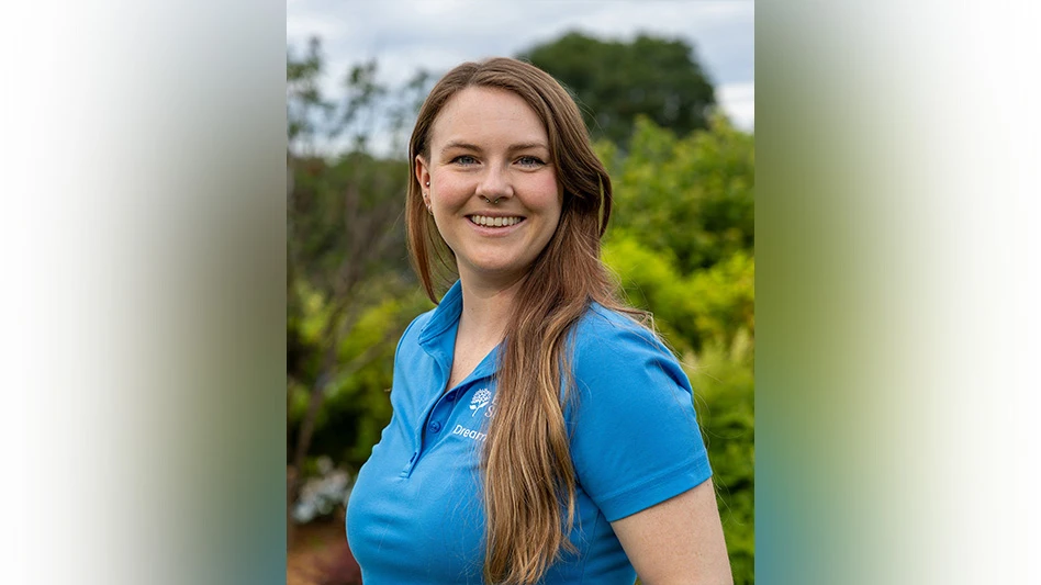 Woman in blue shirt poses in front of greenery