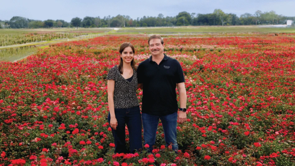 A man and woman stand in a flowering nursery field.
