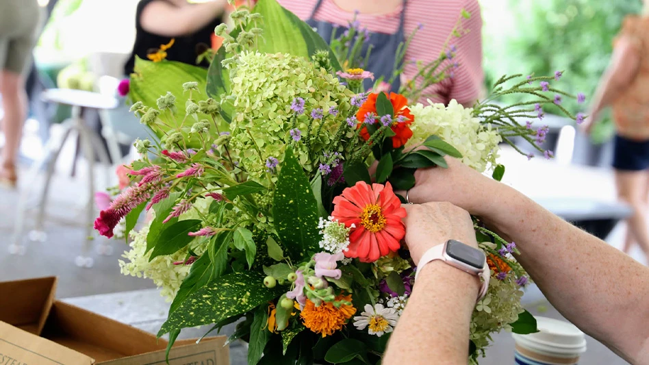 Hands work to arrange cut flowers in vase.