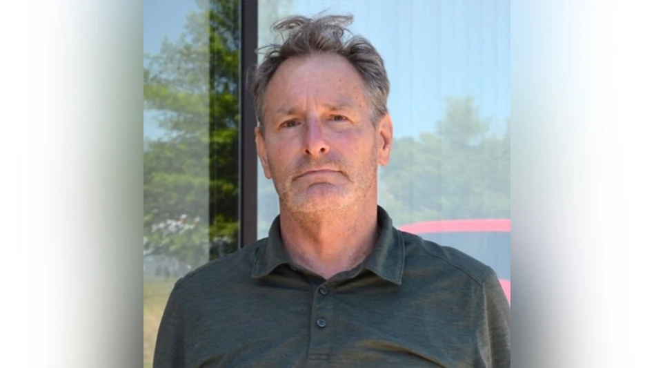 Man posing for headshot in gray shirt in front of window.