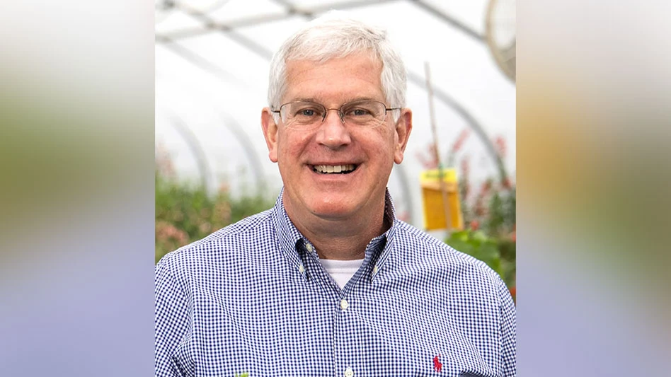 A headshot of a smiling man standing inside a greenhouse.