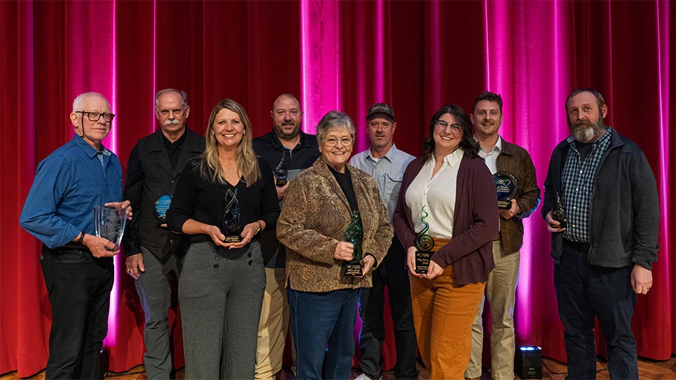 A group of nine smiling people on a stage holding awards.