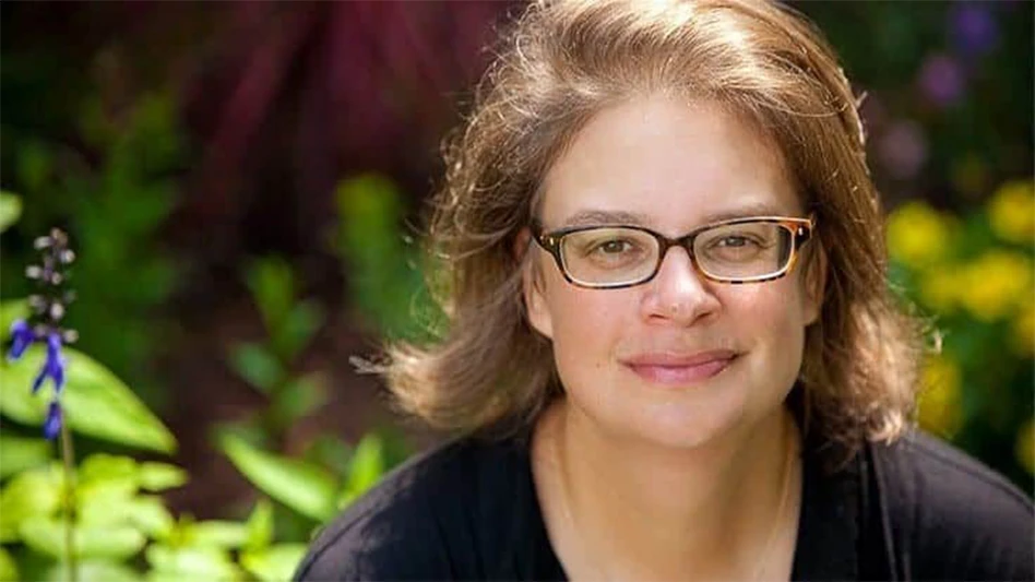 Photo of a woman wearing glasses in a black shirt standing in front of yellow flowers.